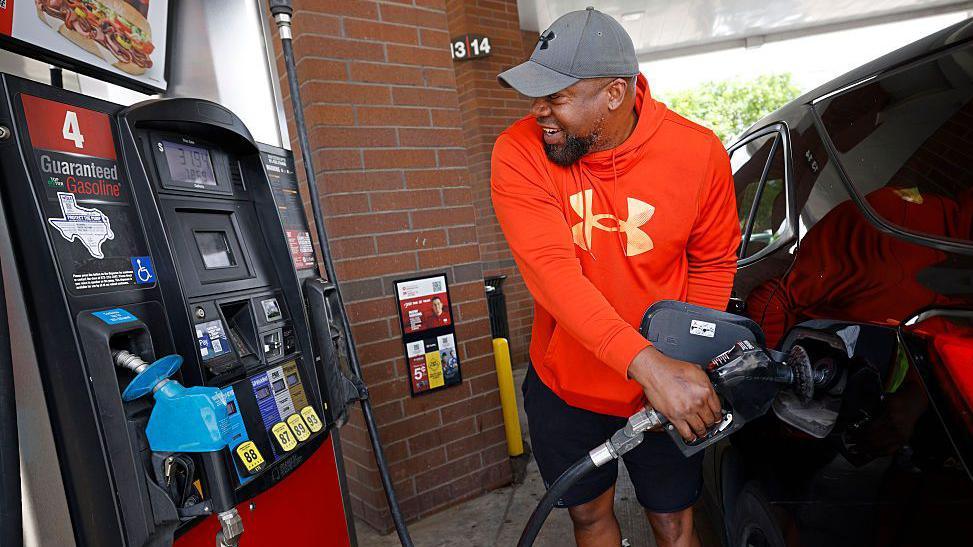 A man in a red hoodie refuels his car while keeping an eye on the price display.