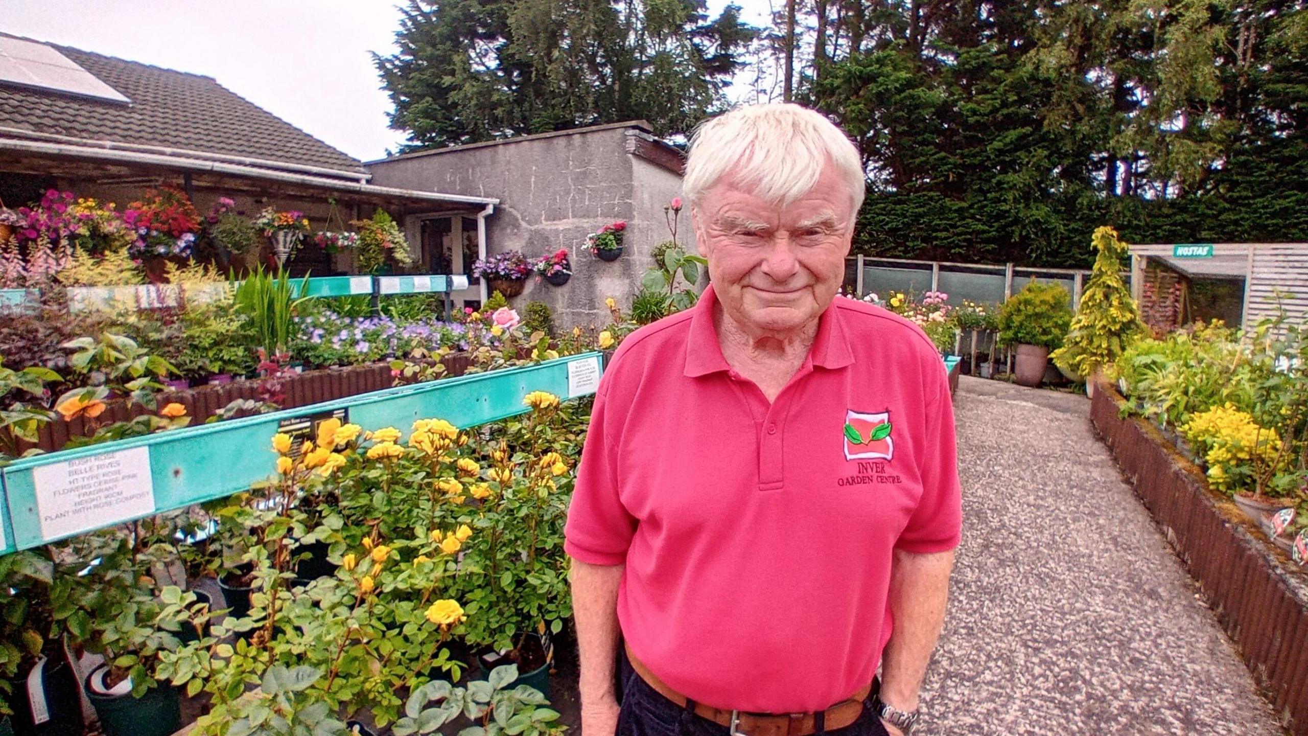 John Shannon. He has white hair, wearing a pink polo top. Plant displays are behind him.