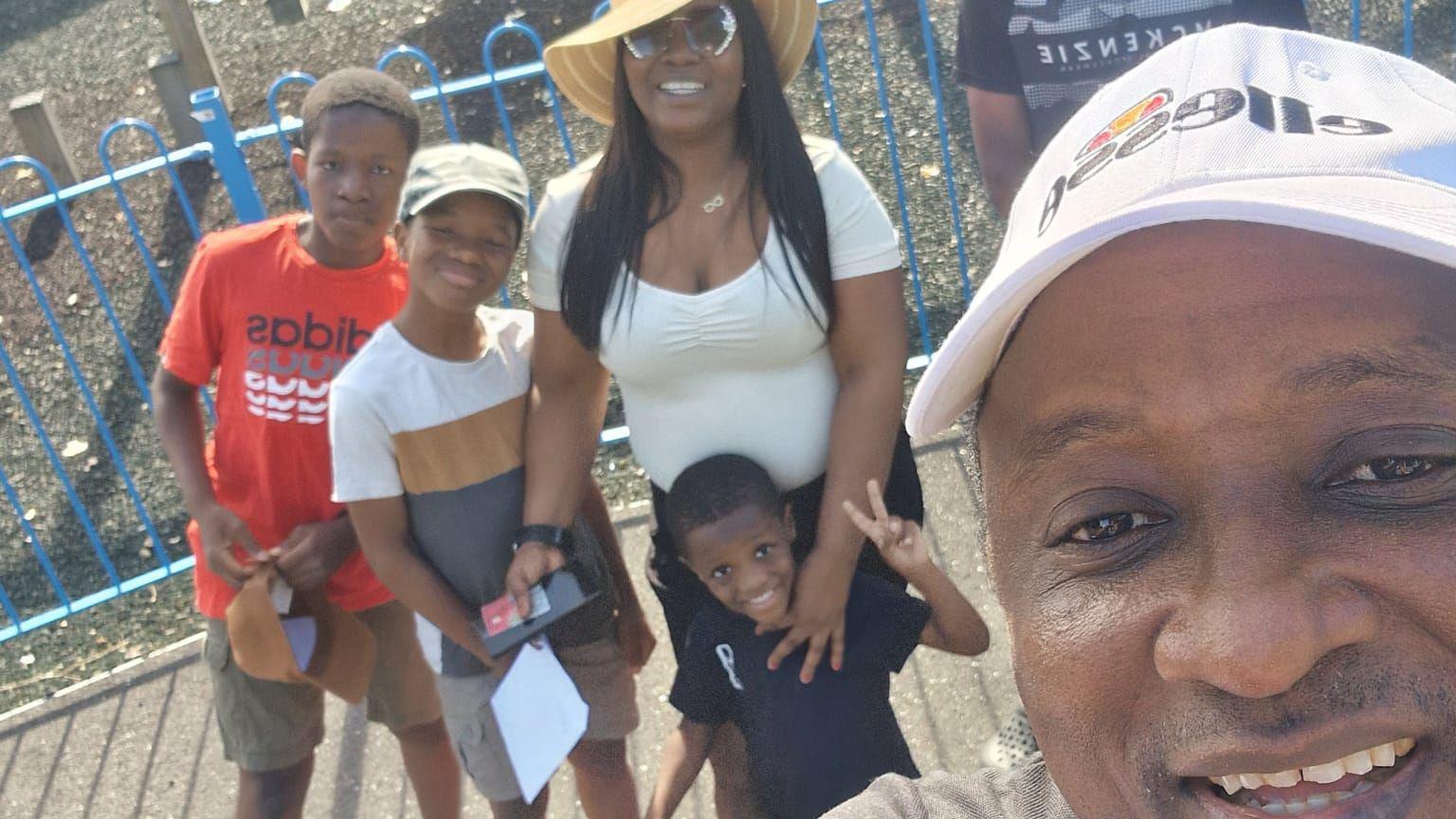 A family selfie with Dad taking the picture in a cap and Mum cuddling four boys in t-shirts