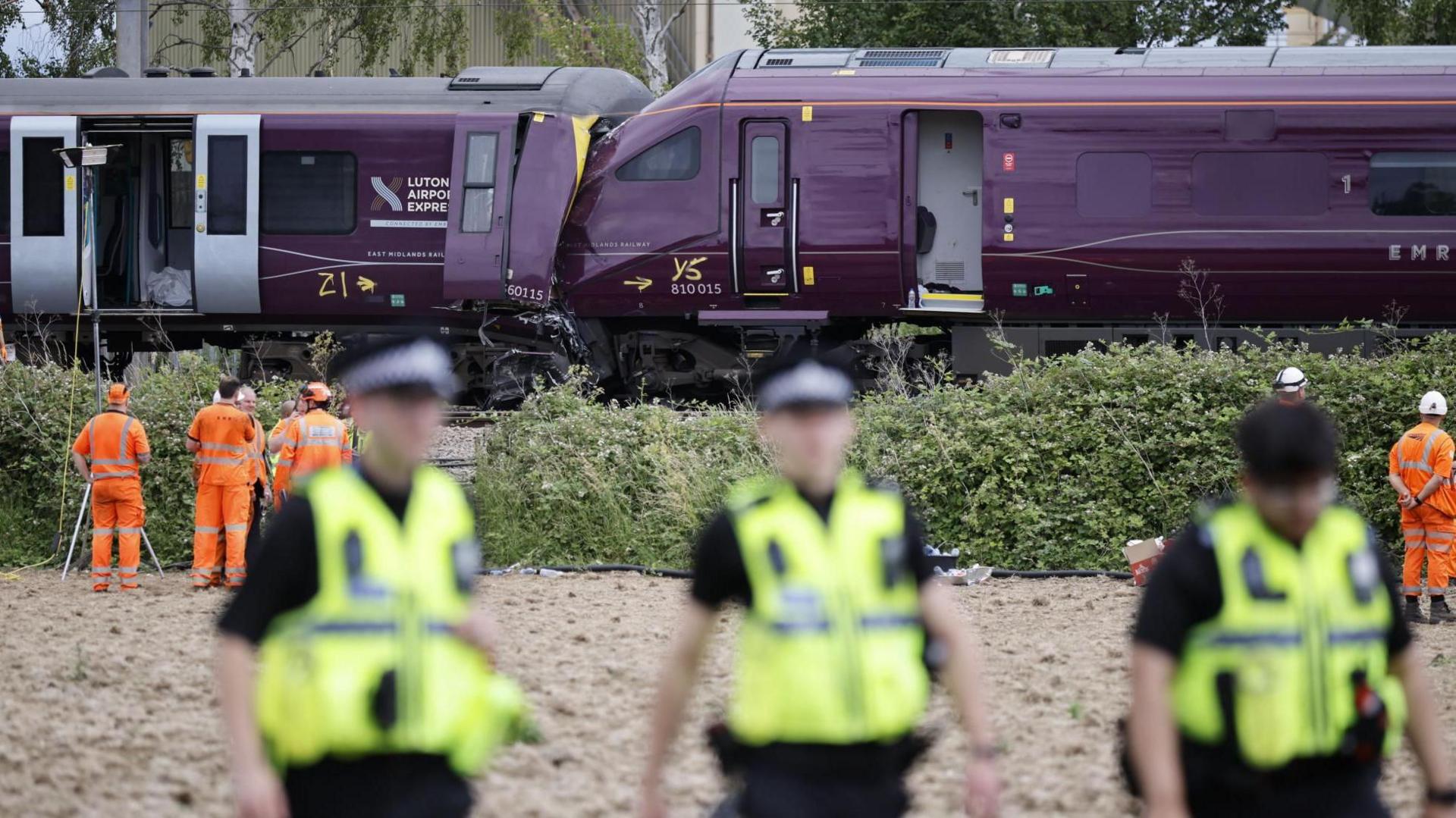 Out of focus emergency workers are stood near two crashed trains behind them.