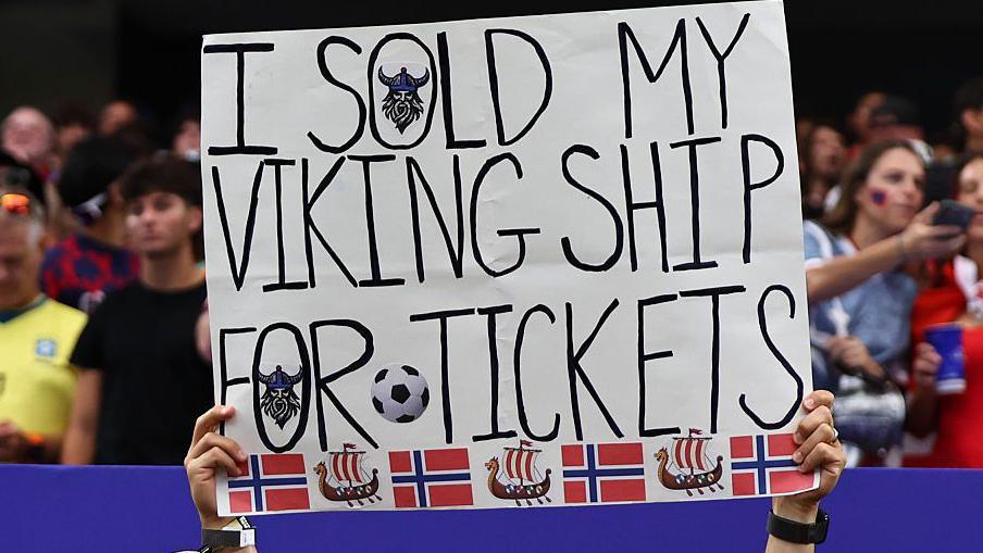 A fan of Norway holds up a sign saying they sold their viking ship for tickets to the match during the FIFA World Cup 2026.