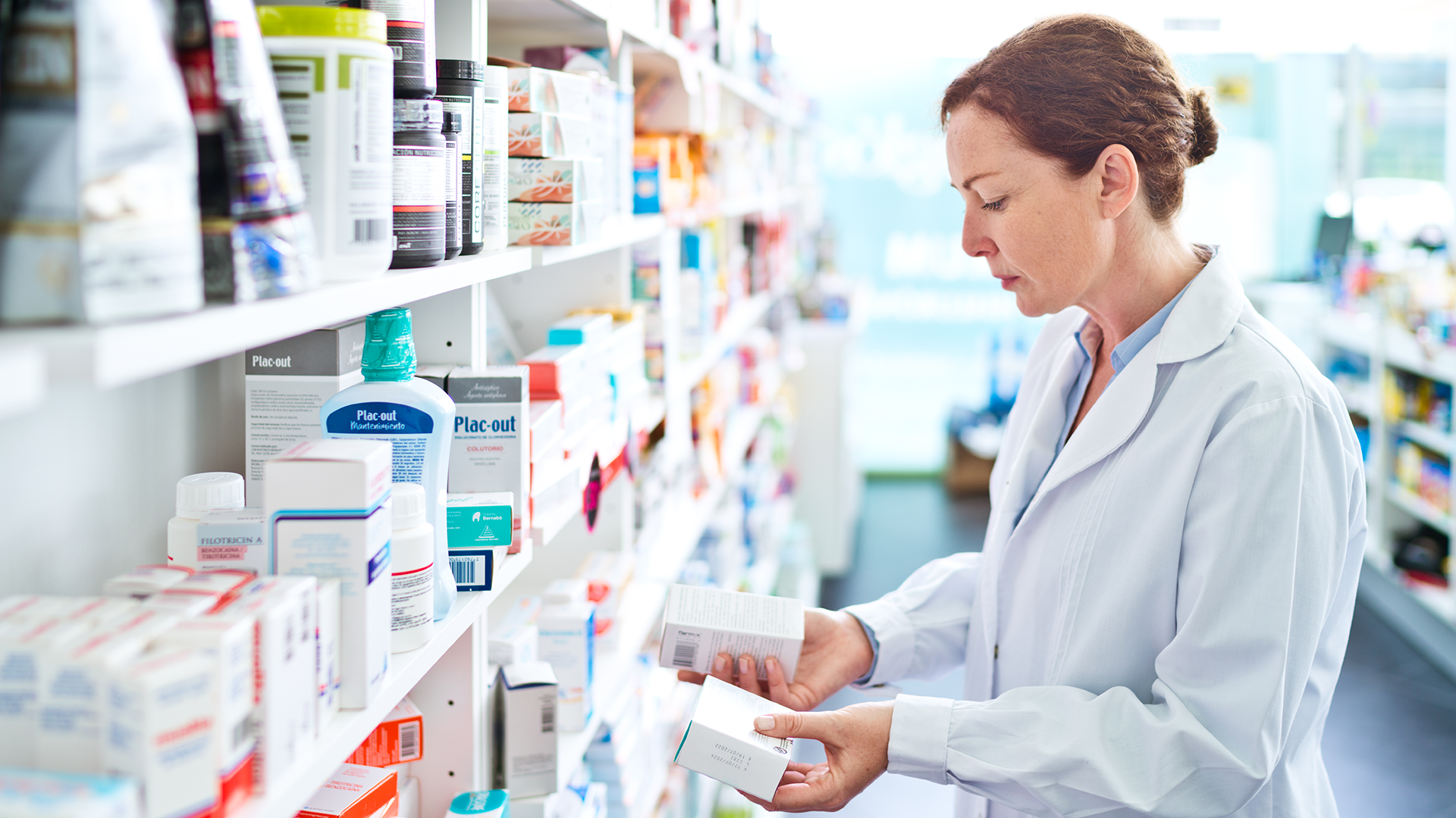 Pharmacist standing in front of shelves in pharmacy, holding medicine boxes in hands.