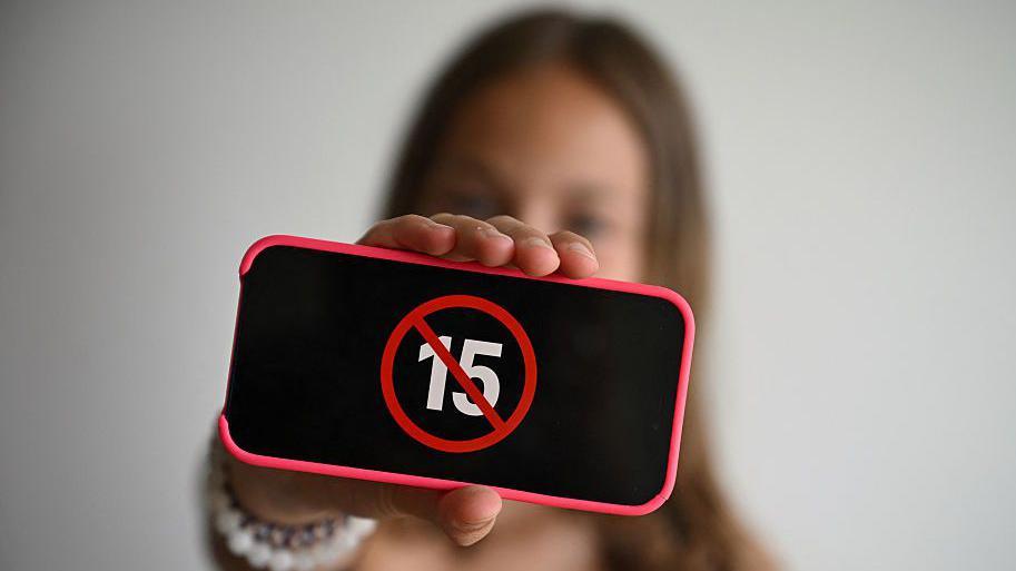 A teenager holds her smartphone displaying a logo "ban under 15" i