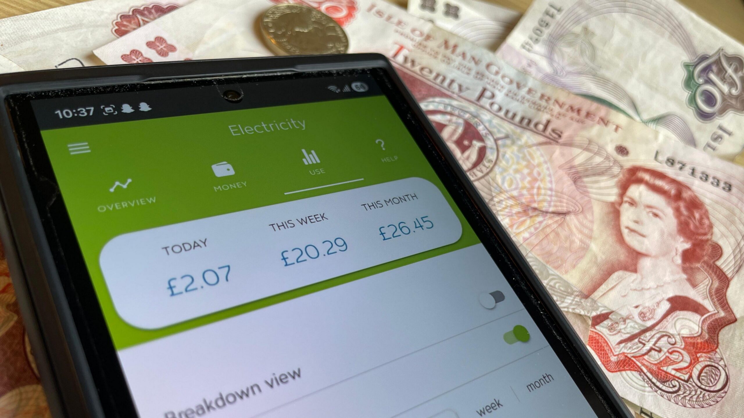 A phone which has an electricity bill up, there is Manx cash in the background.