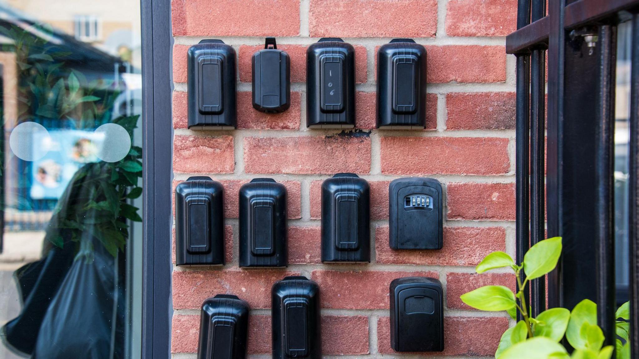 A number of black lockboxes on a wall to the right of a window