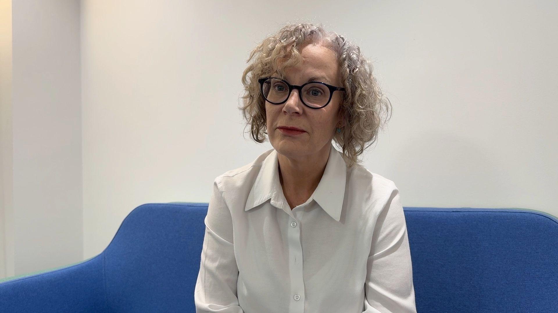 Dr Carmel Corrigan is pictured in the Children's Commissioners office, she is wearing a white shirt and has black glasses.