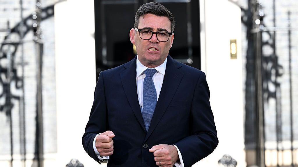 Andy Burnham speaks outside 10 Downing Street after becoming prime minister. He is wearing black glasses, a navy blue suit, white shirt, and blue cotton tie.