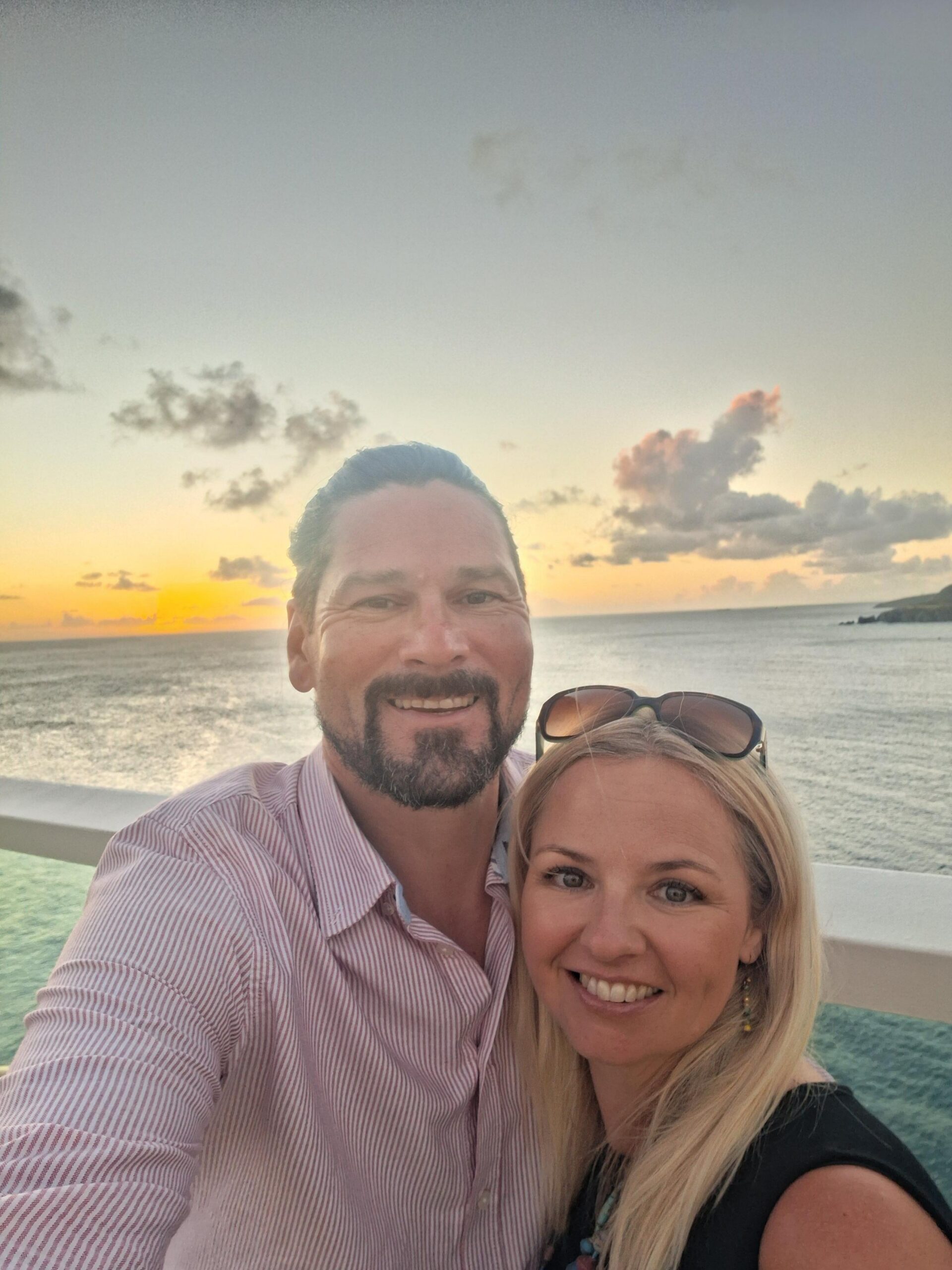 Man and woman smiling in front of the sea and sunset