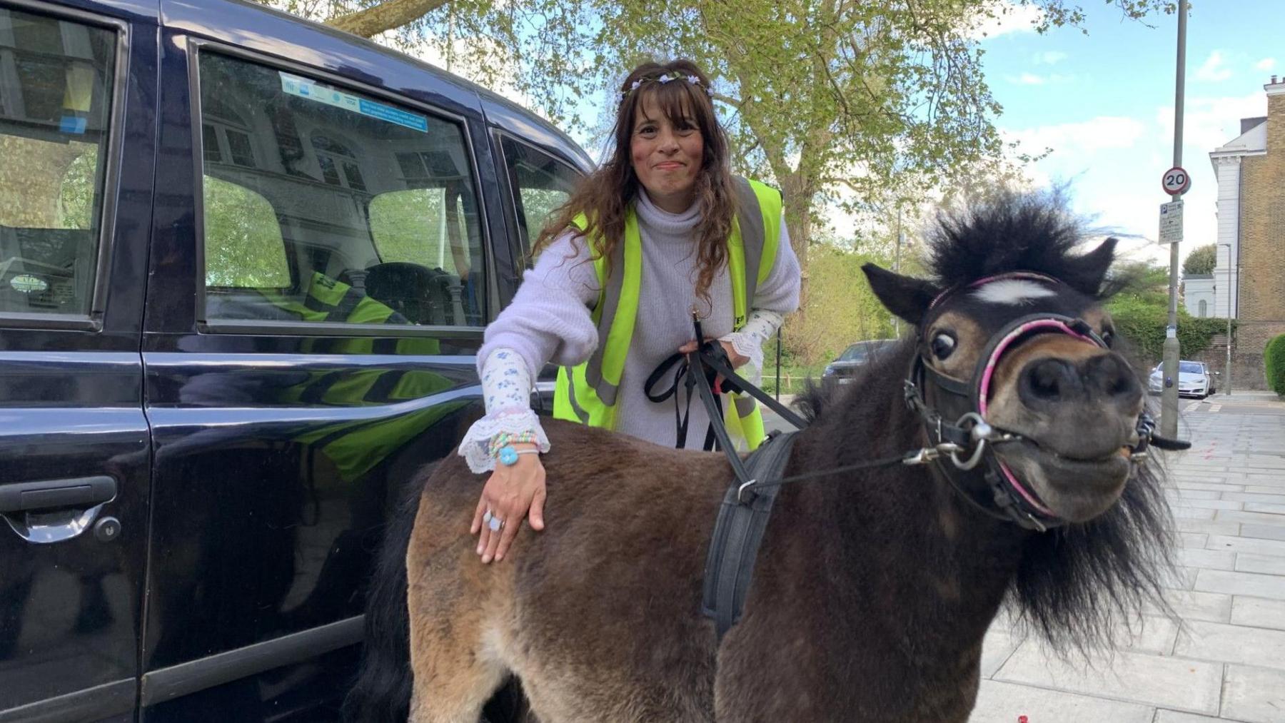 A woman stood behind a miniature pony next to a black taxi