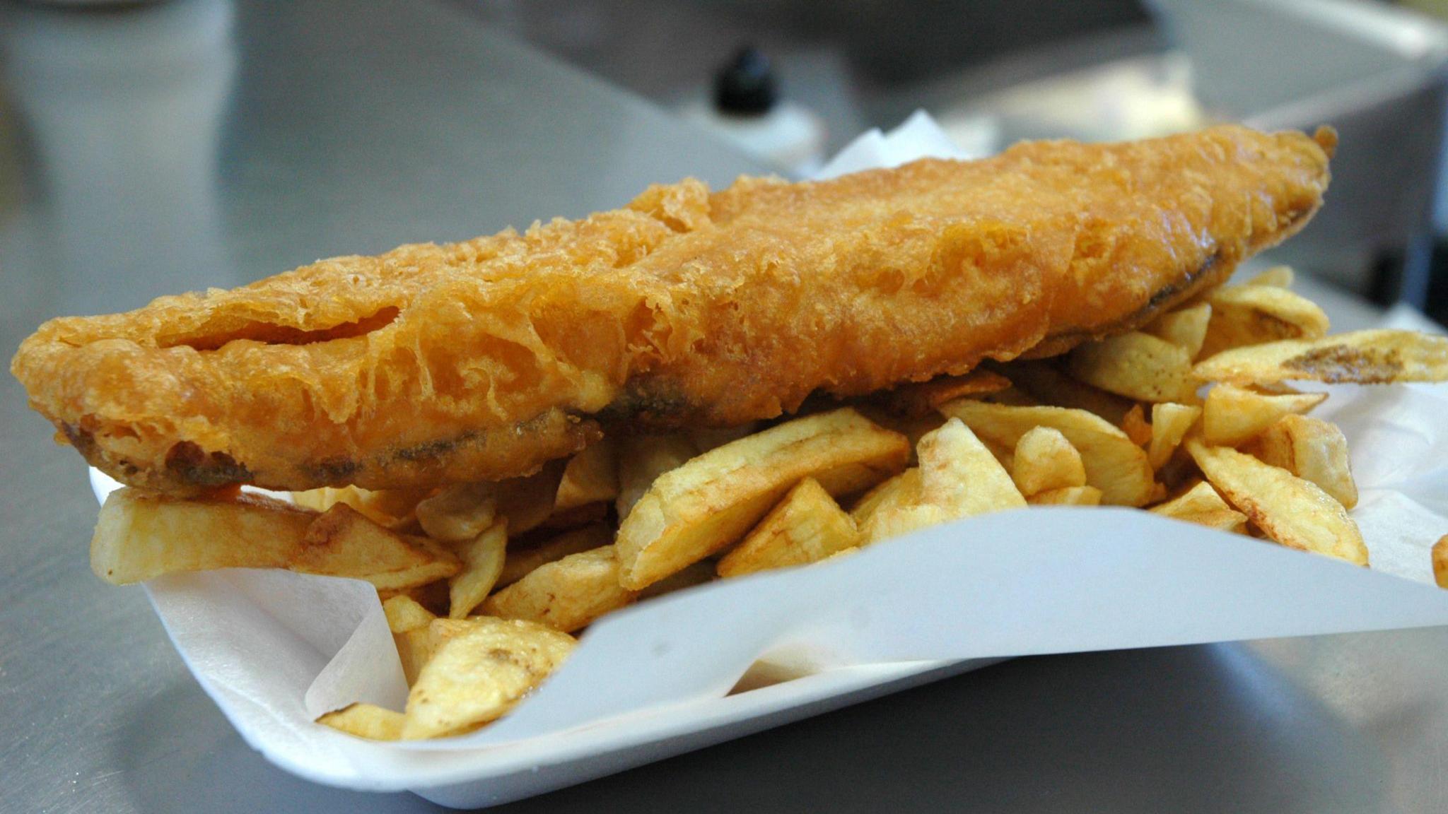 A white tray containing a portion of battered fish and chips.