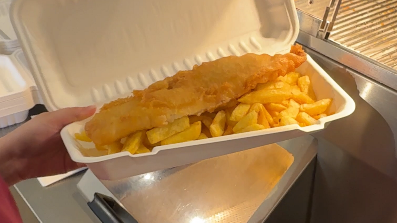 A battered fish and chips in a paper packet.