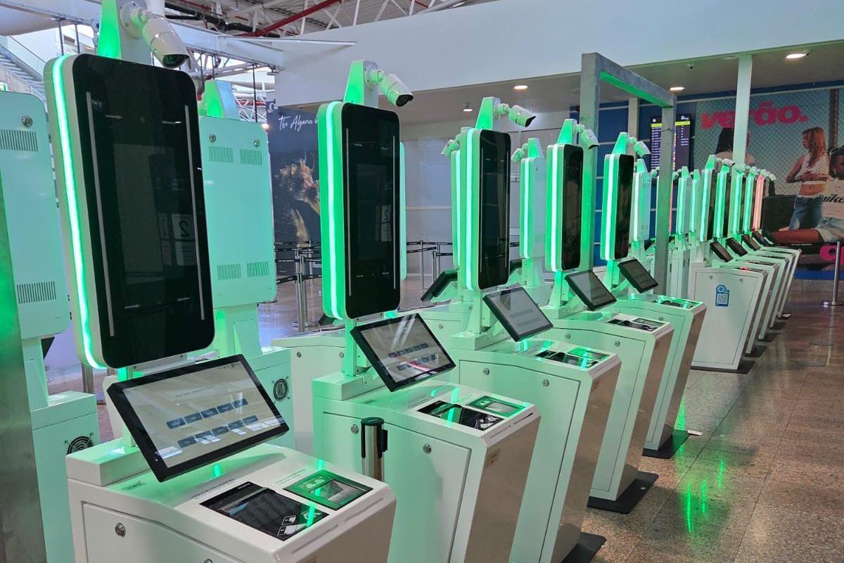 A row of automated machines with screens and equipment to record facial scans, fingerprints and scan passports. They have green lighting.