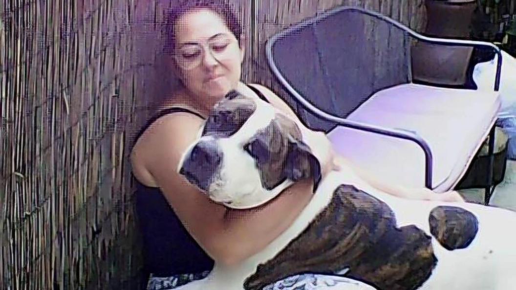 Eve holds American Bulldog Khan in her arms while sitting on a chair in the garden.