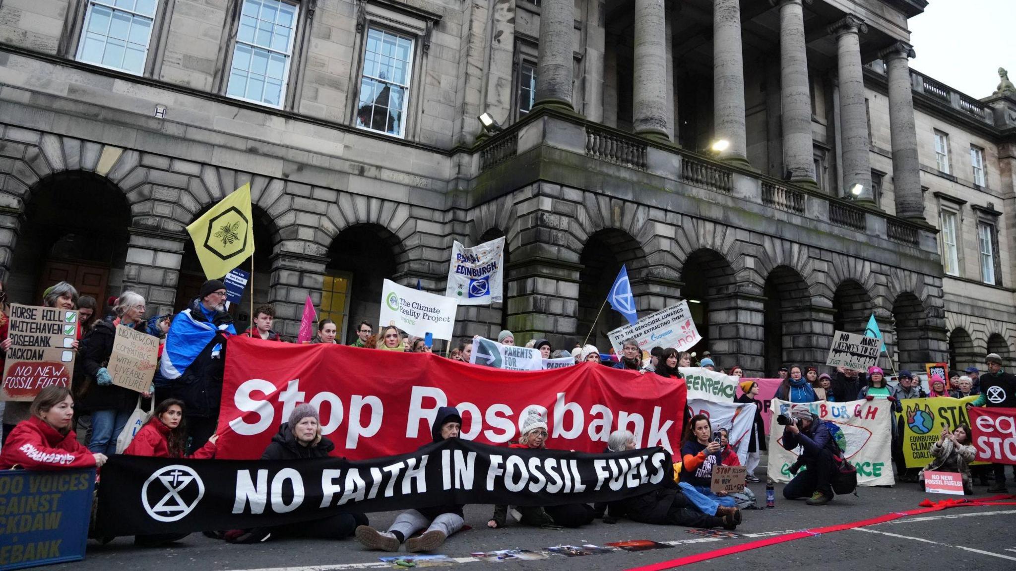 Protestors holding anti-fossil fuel banners gather under the colonnades of the Court of Session building. One reads 'Stop Rosebank'.
