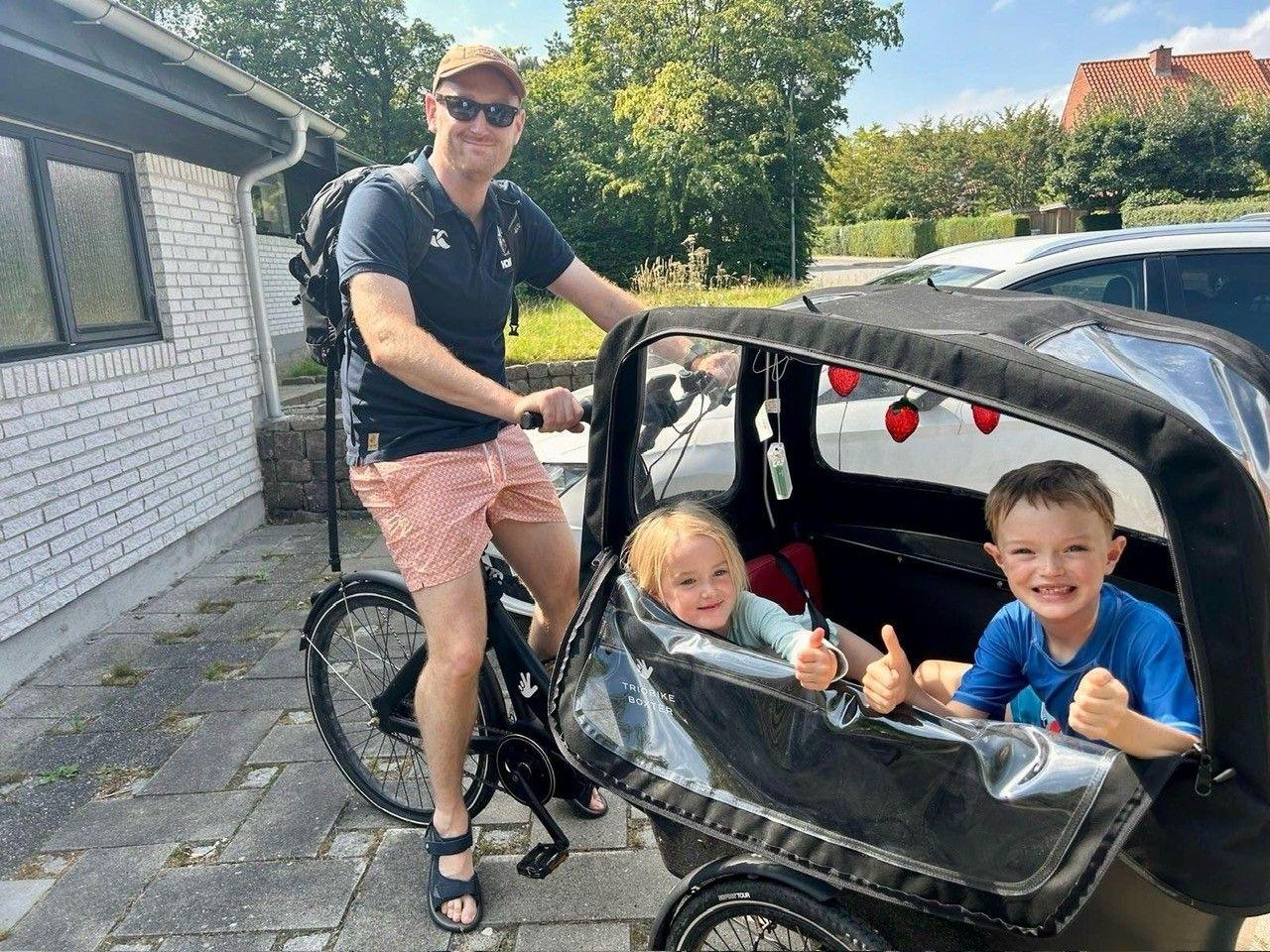 Henry Vanderpump sits on an electric bike with a cart on the front carrying his two children