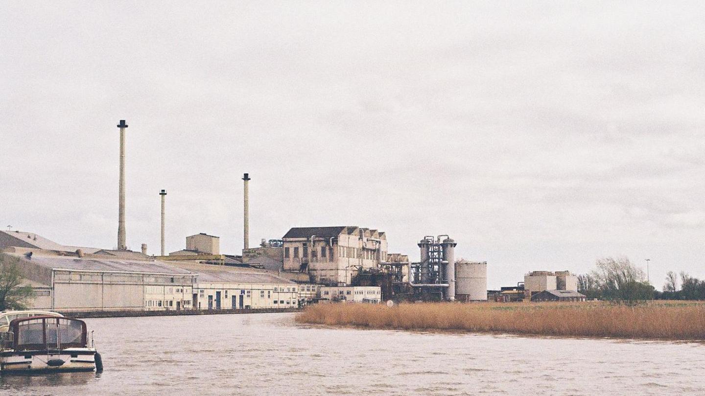 Looking at the Cantley sugar factory from upstream, with its buildings, the river and a boat in view