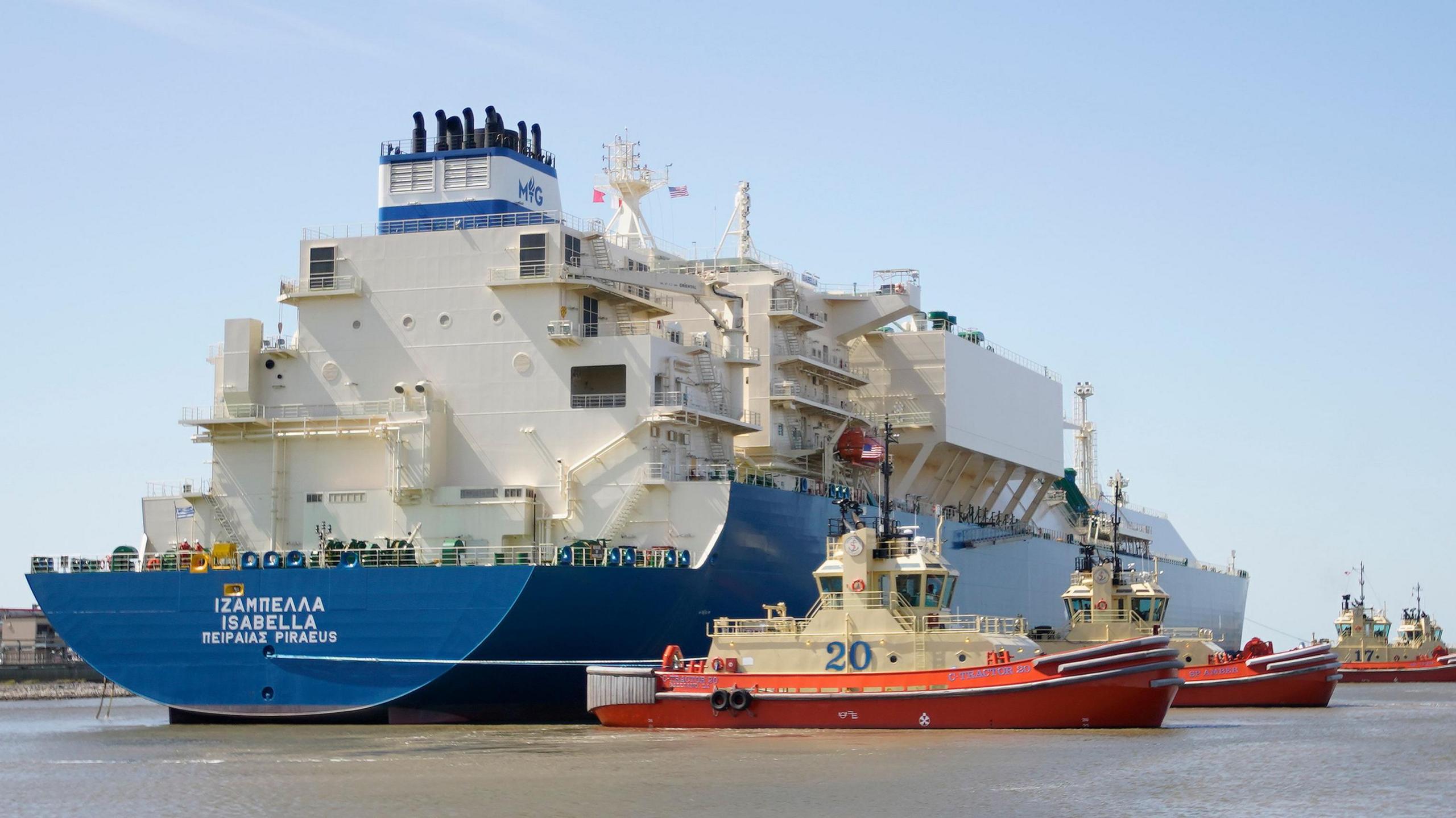 A huge, blue and white tanker ship being moved into position in Cameron Parish by white, orange and red tug boats