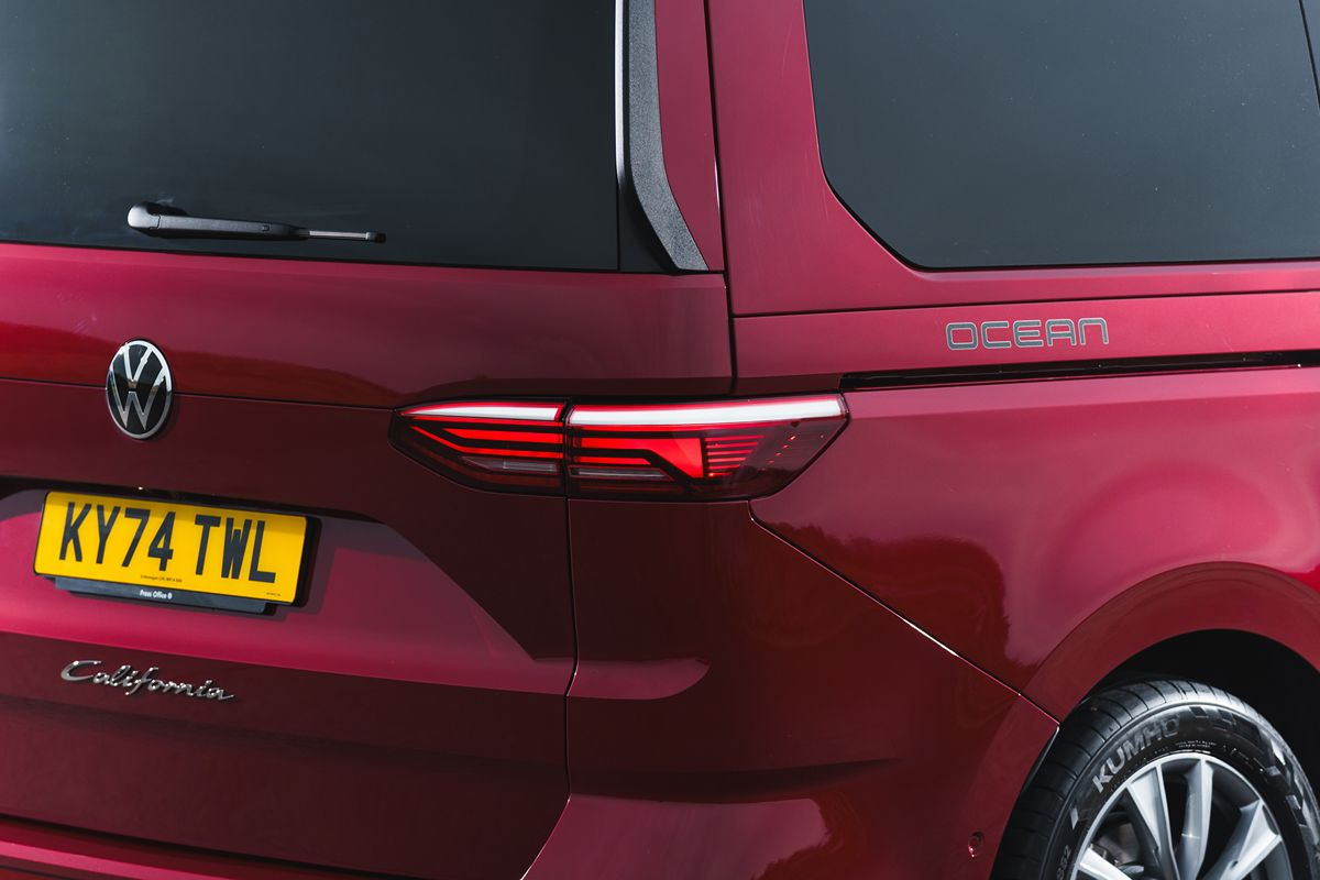 Rear view of a red Volkswagen California Ocean camper van, showing the taillight, VW logo, and license plate.